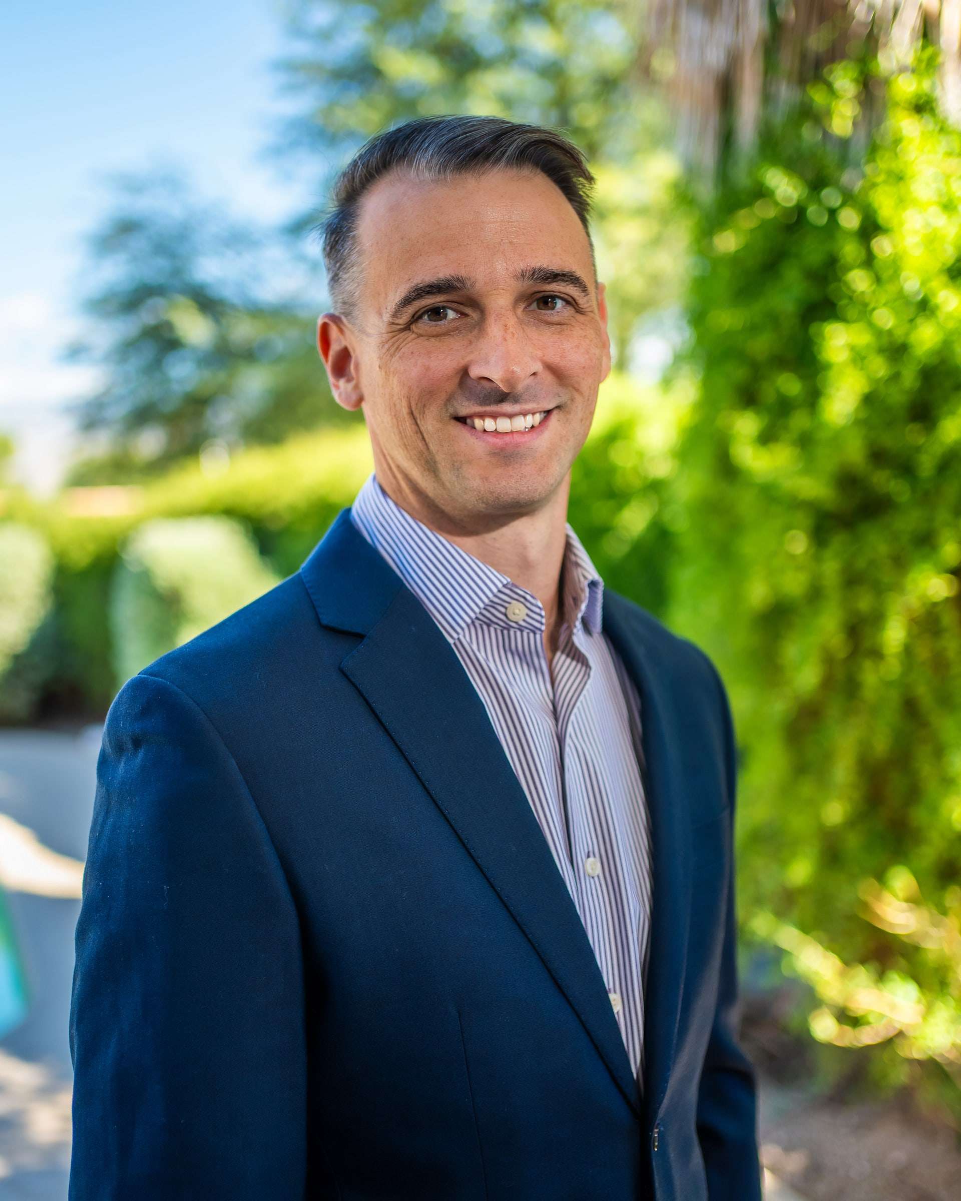 Kyle Witt, MD, internal medicine physician, smiling outdoors in a navy suit jacket.